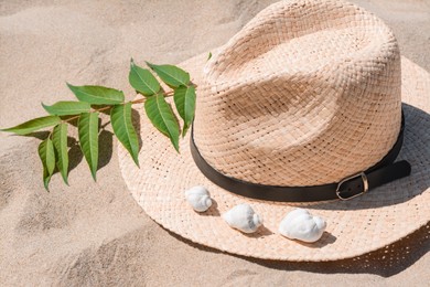 Straw hat, seashells and green leaves on sandy beach, closeup view
