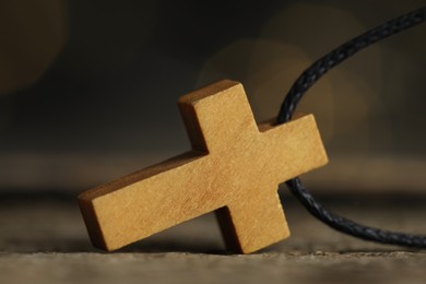 Christian cross on wooden table against blurred background, closeup