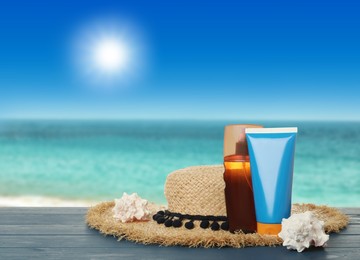 Skin sun protection products and hat on blue wooden table against seascape. Space for design