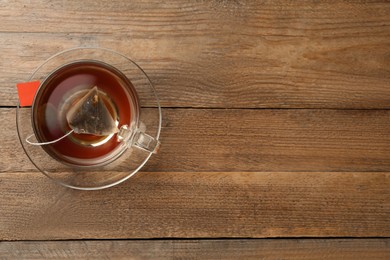 Tea bag in glass cup of hot water on wooden table, top view. Space for text