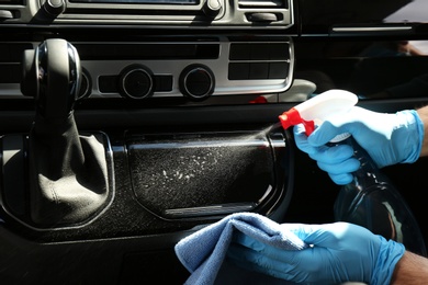 Man in gloves cleaning car dashboard with disinfectant spray and rag, closeup. Preventive measure during coronavirus pandemic