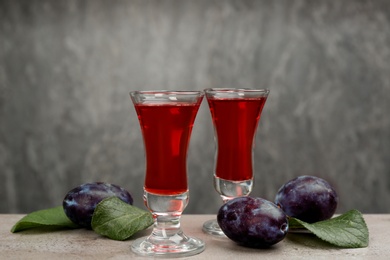 Delicious plum liquor and ripe fruits on table against grey background. Homemade strong alcoholic beverage