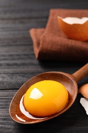 Spoon with raw egg yolk on black wooden table, closeup