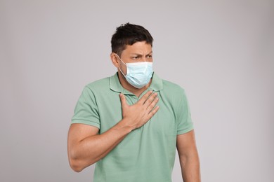 Man in medical mask suffering from pain during breathing on grey background