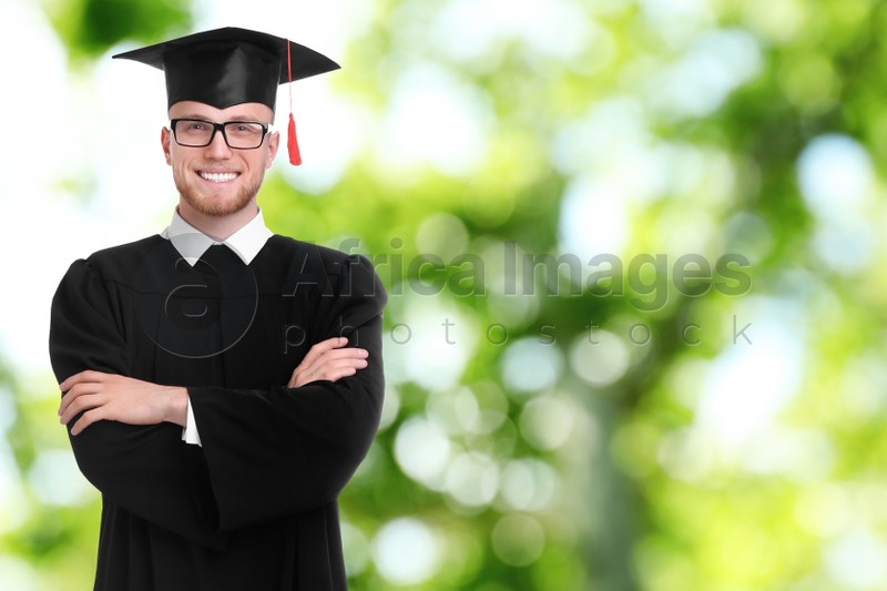 Happy student wearing graduation hat on blurred background, space for text