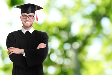 Happy student wearing graduation hat on blurred background, space for text
