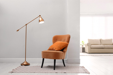Comfortable orange armchair with cushion in stylish room interior