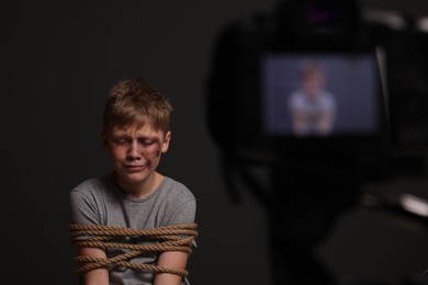 Photo of Little boy with bruises tied up and taken hostage near camera on dark background, selective focus