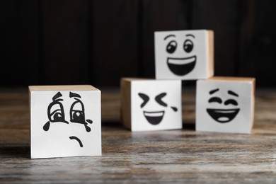Cubes with sad and funny faces on wooden table. Bullying concept