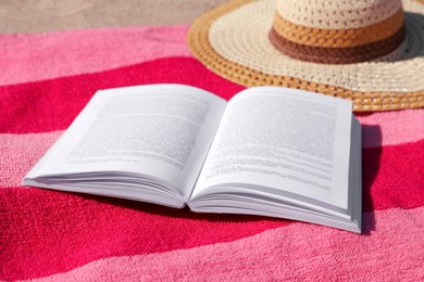 Photo of Open book, hat and striped towel on sandy beach