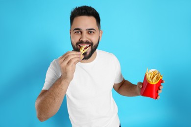 Young man eating French fries on light blue background