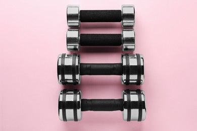Photo of Dumbbells on light pink background, flat lay. Weight training equipment