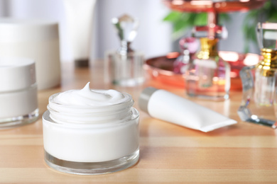 Open jar of cream on wooden dressing table. Space for text