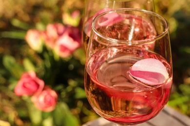 Photo of Glass of delicious rose wine with petals outside, closeup. Space for text