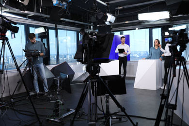 Photo of Presenters, makeup artist and video camera operator working in studio. News broadcasting