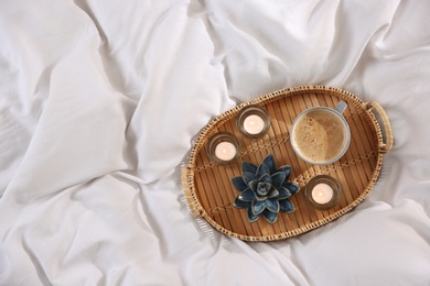 Wicker tray with cup of coffee and candles on soft white blanket, top view