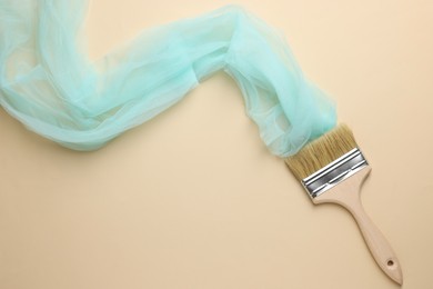 Photo of Brush painting with light blue tulle on beige background, top view. Creative concept