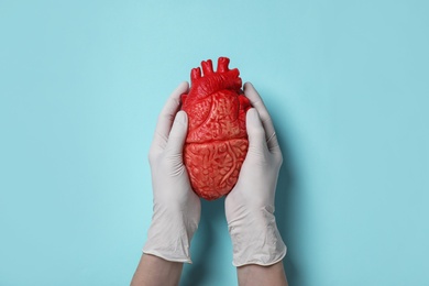 Doctor holding heart model on cyan background, top view