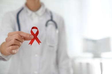 Doctor holding red ribbon on blurred background, closeup with space for text. AIDS awareness month