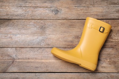 Yellow rubber boot on wooden background, top view. Space for text