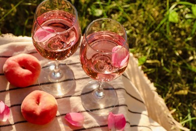 Photo of Glasses of delicious rose with petals wine and peaches on white picnic blanket outside, above view