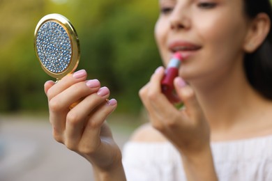 Woman with cosmetic pocket mirror applying lipstick outdoors, closeup