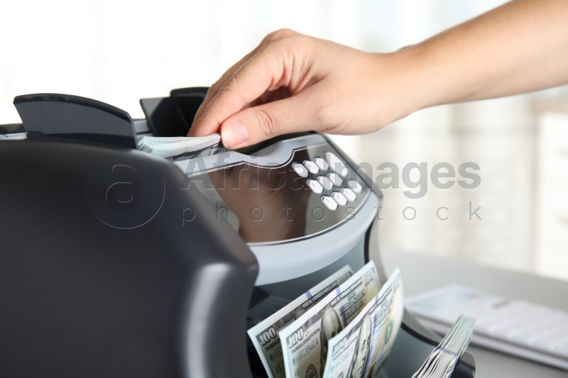 Woman putting money into counting machine at table indoors, closeup