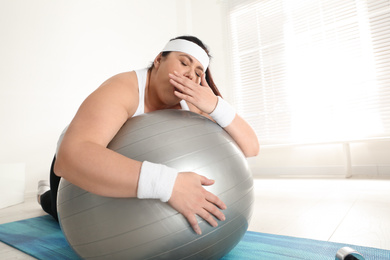 Lazy overweight woman leaning on fit ball instead of training at gym