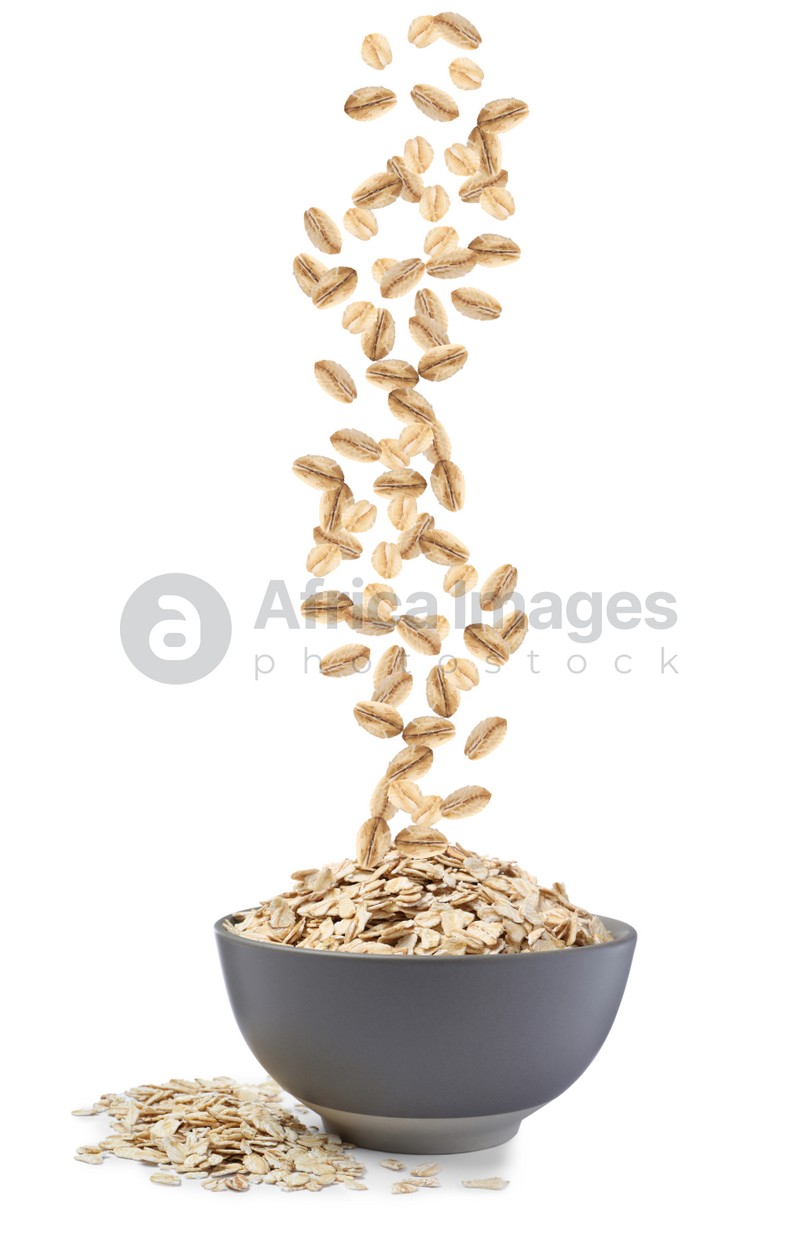 Dry uncooked oatmeal falling into bowl on white background