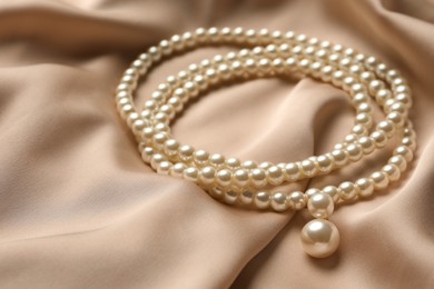 Photo of Elegant necklace with pearls on beige silk, closeup