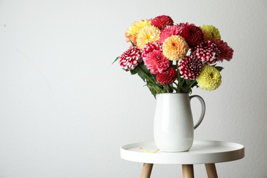 Photo of Bouquet of beautiful dahlia flowers on table near white wall. Space for text