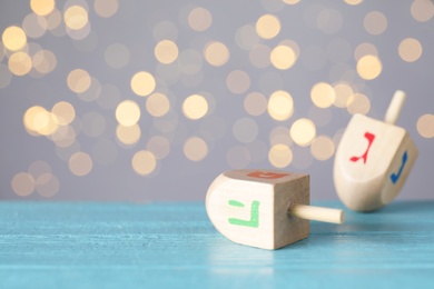 Hanukkah traditional dreidel with letters Pe and He on wooden table against blurred lights. Space for text
