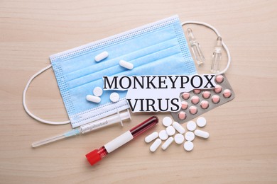 Card with words Monkeypox Virus, medical mask, different pills, syringe and test tube on wooden table, flat lay