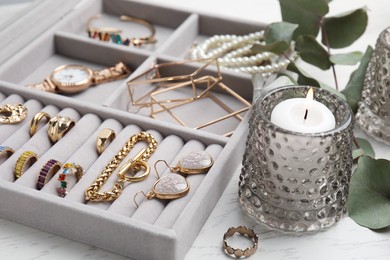 Elegant jewelry box with beautiful bijouterie and burning candle on white wooden table, closeup