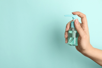 Woman holding antiseptic gel on light blue background, closeup. Space for text