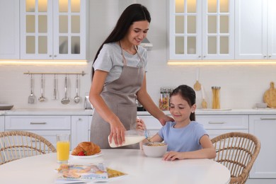Happy mother adding milk to her daughter's cereal in kitchen. Single parenting