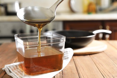 Photo of Pouring used cooking oil with ladle into container on wooden table in kitchen
