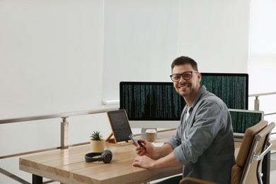 Happy programmer with smartphone working at desk in office