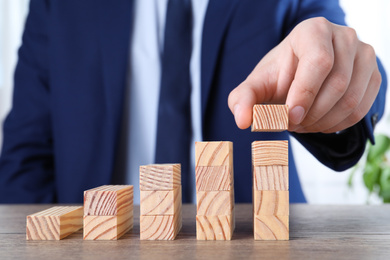 Photo of Businessman building steps with wooden blocks on table, closeup. Career ladder