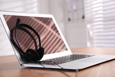 Modern laptop with headset on wooden table in office, space for text. Hotline service
