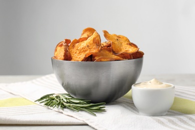 Bowl of sweet potato chips with sauce and rosemary on table against light background