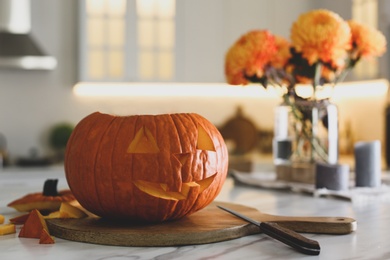 Pumpkin jack o'lantern on white marble table in kitchen, space for text. Halloween celebration