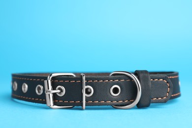 Black leather dog collar on light blue background, closeup. Space for text