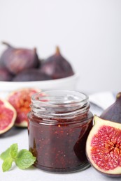 Photo of Glass jar of tasty sweet fig jam and fruits on light table