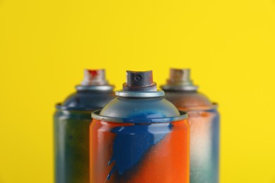 Used cans of spray paints on yellow background, closeup