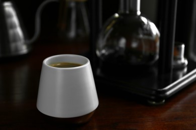 Photo of Cup with coffee and vacuum maker on wooden table in cafe