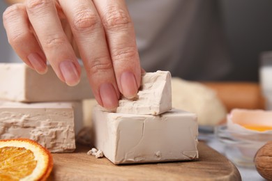 Photo of Woman taking piece of compressed yeast at table, closeup