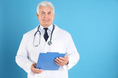 Portrait of senior doctor with clipboard against blue background, space for text