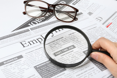 Woman looking through magnifying glass at newspaper, closeup. Job search concept