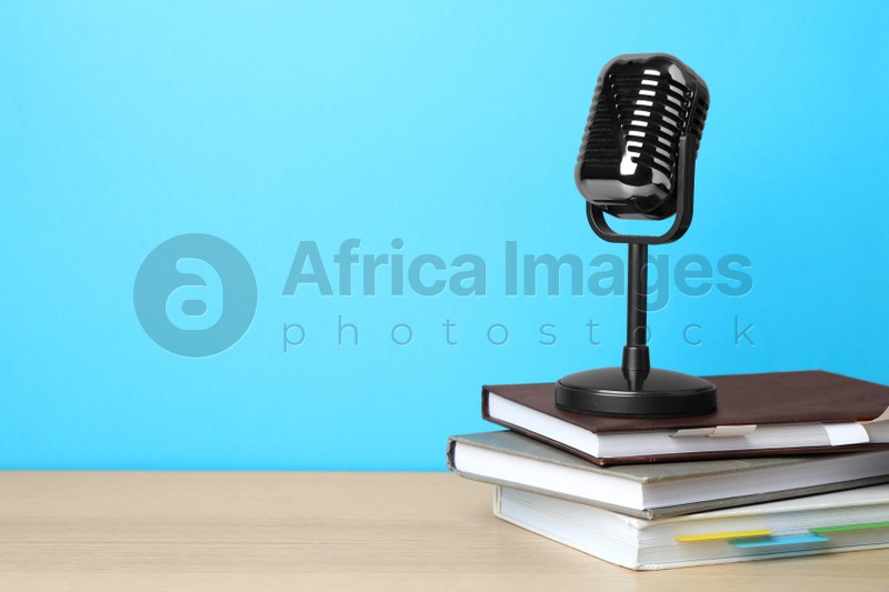 Photo of Retro microphone and notebooks on wooden table against light blue background, space for text. Job interview